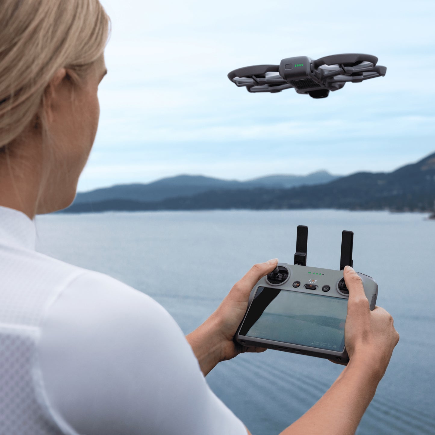 Woman operating a DJI Avata 360 drone with a RC 2 controller by a lake