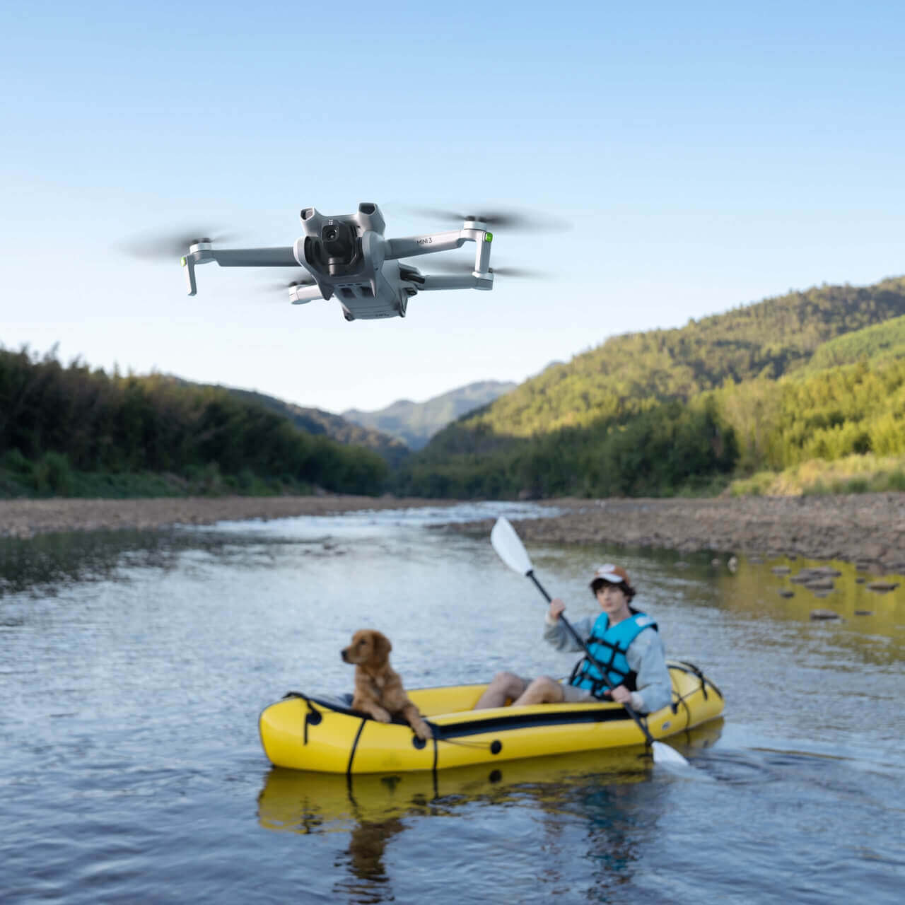 A person kayaking with a dog, as a DJI Mini 3 drone flies above, capturing the scenic river landscape.