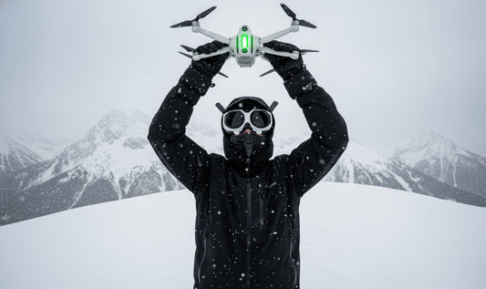 a full shot of a man dressed in winter attire holding a Insta360 Antigravity A1 drone like a trophy in the air whilst wearing the matching FPV goggles in front of a snowy mountain landscape