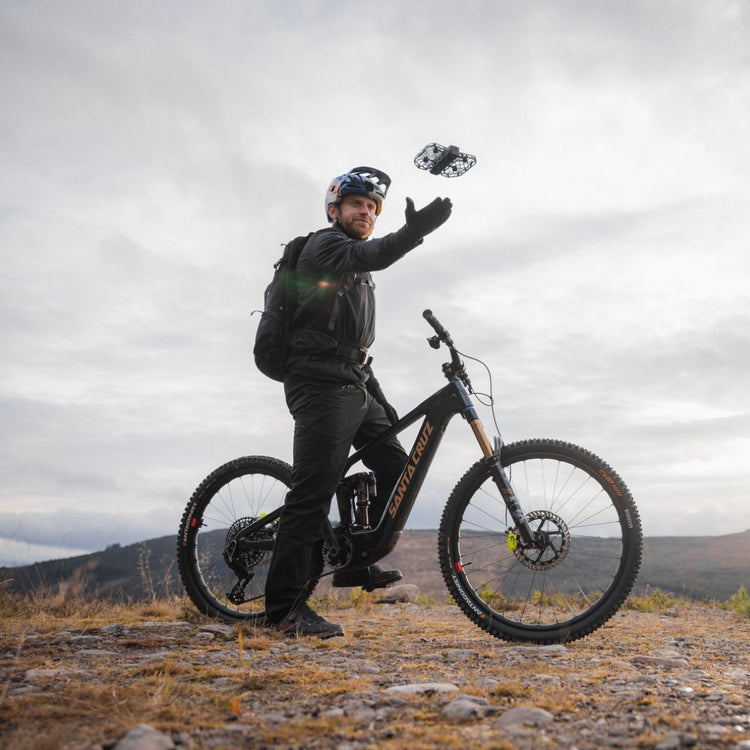 man in biking gear holding his electric bike while doing a palm takeoff with the HOVERAir X1 fly more combo black