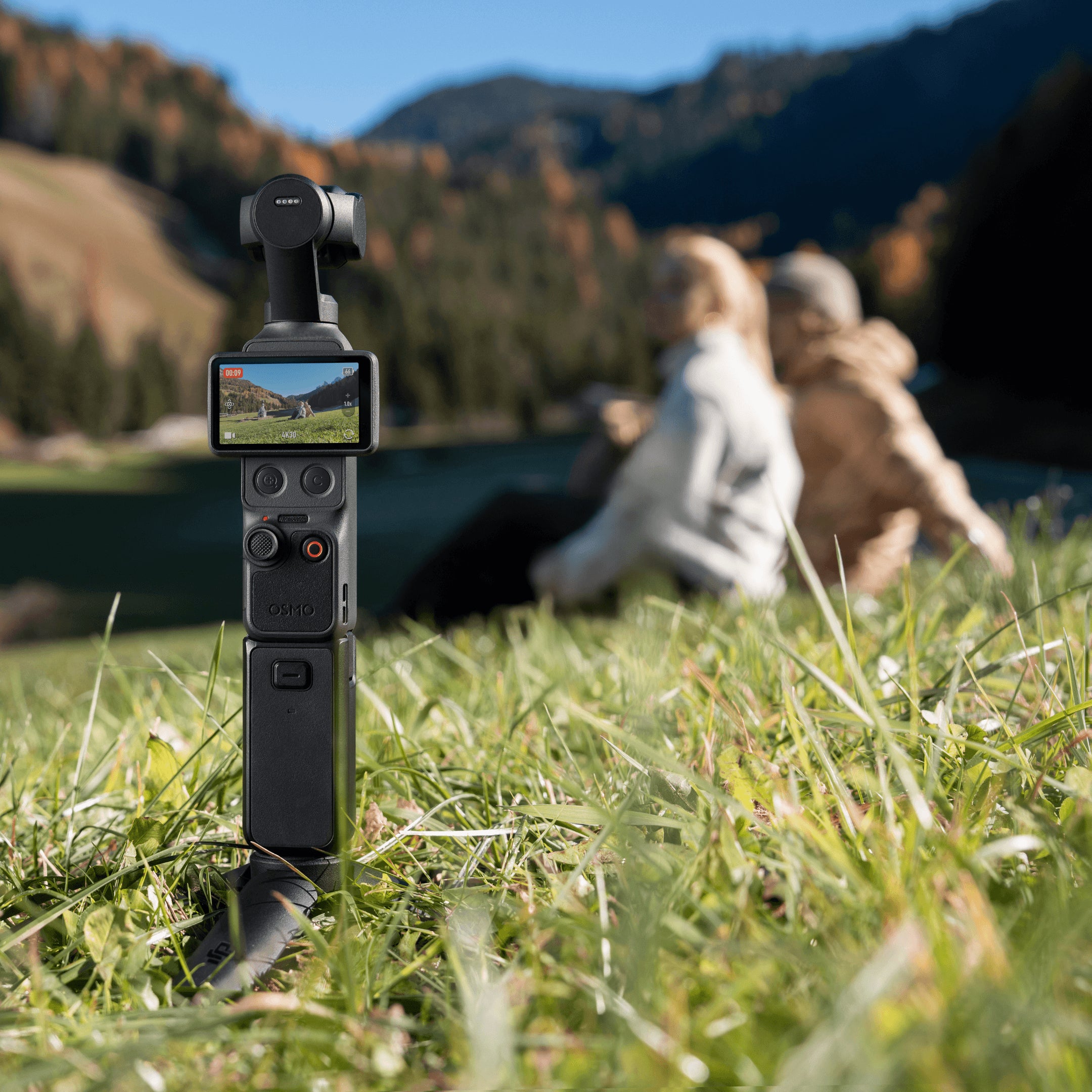 DJI Osmo Pocket 4 Creator Combo standing in grass capturing a scenic view with creators in the background.