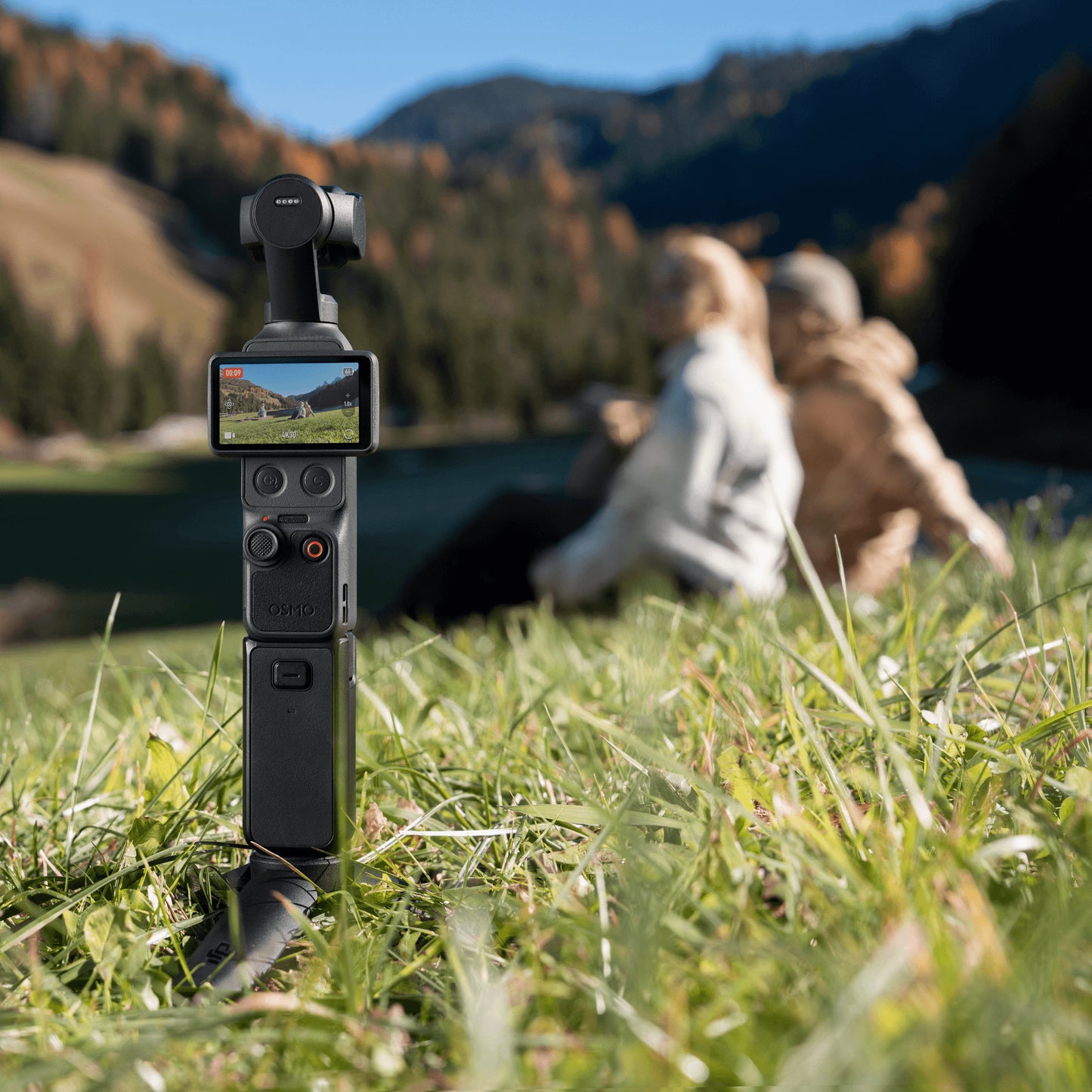DJI Osmo Pocket 4 Creator Combo standing in grass capturing a scenic view with creators in the background.