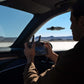 Person inside a vehicle using a DJI RC 2 control with a desert landscape outside and a DJI Avata 360