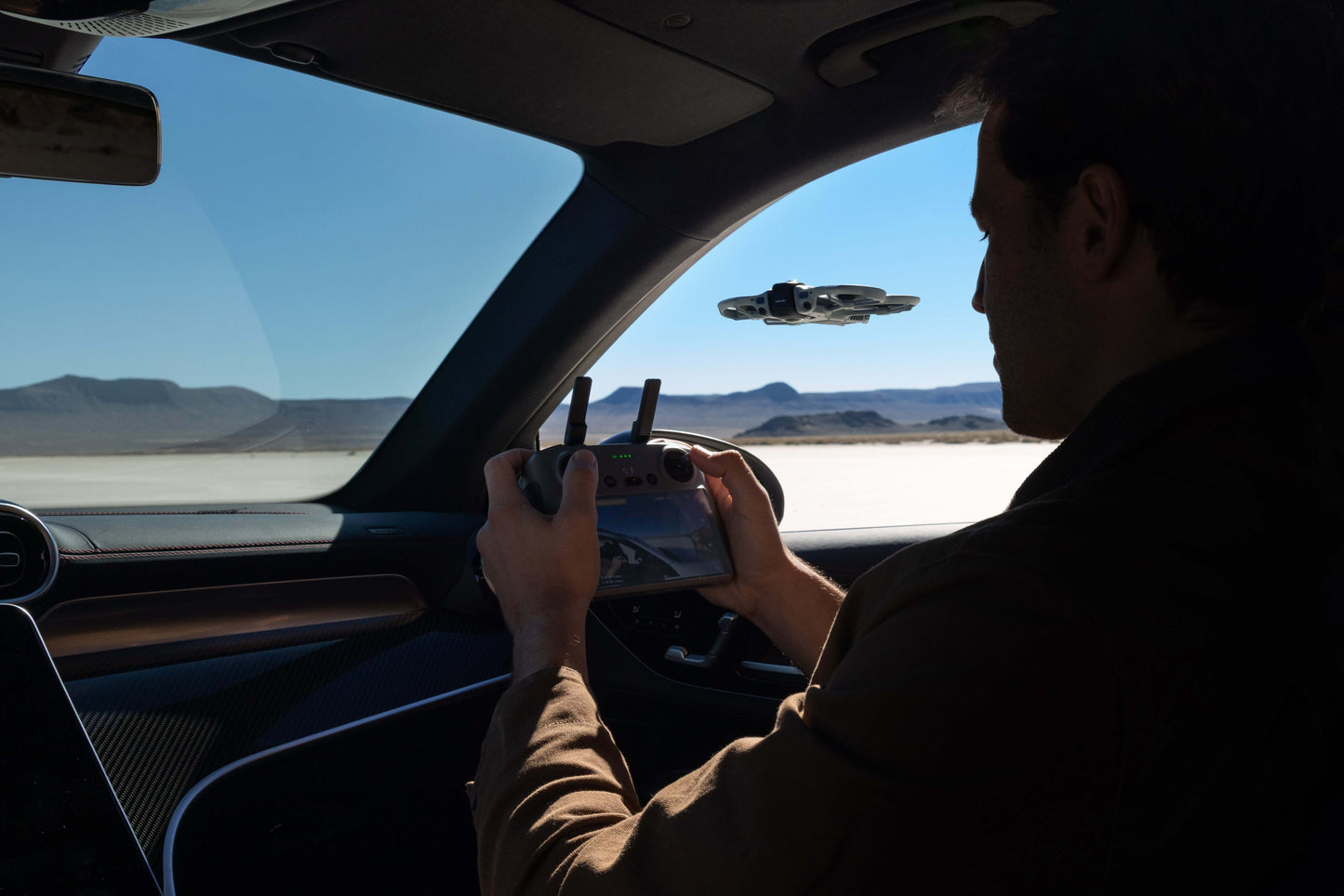 Person inside a vehicle using a DJI RC 2 control with a desert landscape outside and a DJI Avata 360